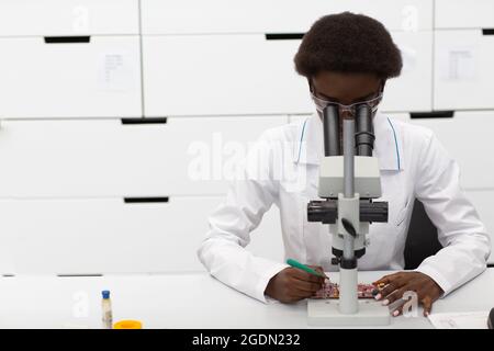 Scientist african american woman working in laboratory with electronic tech instruments and microscope front view. Research and development of electronic devices by color black woman. Stock Photo