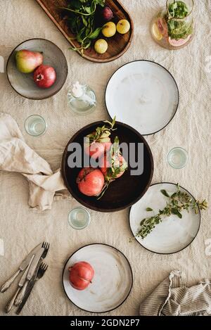 Fall table styling concept. Flat-lay of dinnerware with fresh seasonal fruits, drink in jug, dried flowers and glasses over beige linen tablecloth, to Stock Photo