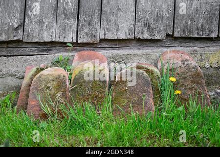Old, vintage, rustic roof tiles in the green, spring colored grass, covered by moss, against a textured, wooden wall Stock Photo