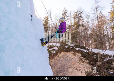 Female ice climber going down an ice waterfall, using a safety top rope. Stock Photo