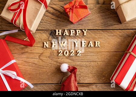 Happy New Year 2022. Quote made from wooden letters and numbers 2022 on wooden background with multicolored gift boxes. Creative concept for new year Stock Photo
