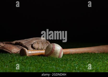 Old baseball bat and mitt low angle selective focus on grass field and dark background Stock Photo