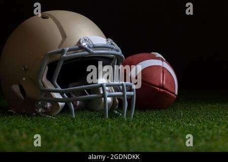 Low angle selective focus of football and gold helmet on grass with dark background Stock Photo