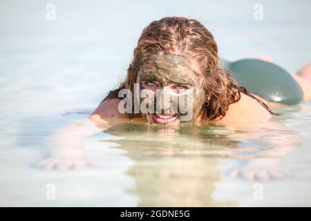 Mud covered Caucasian tourist floats in the Dead Sea, Israel Stock Photo