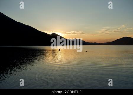 Peaceful lake horizon at sunset with late evening swimmers having a last swim in clear Alpine water, Fuschl lake, Fuschl am See, Austria Stock Photo
