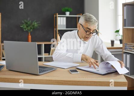 Busy senior businessman checks documents while working sitting in his own office. Stock Photo