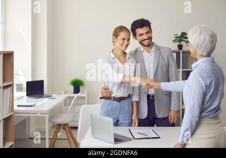 Smiling couple shaking hands with bank manager, real estate agent or loan advisor Stock Photo