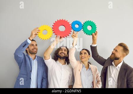 Smiling diverse colleagues connect cogwheel look for solution Stock Photo