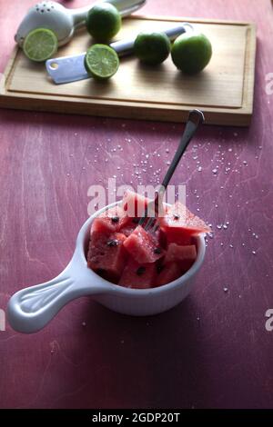 Vertical shot of a bowl of delicious watermelon slices with limes next to it on a cutting board Stock Photo