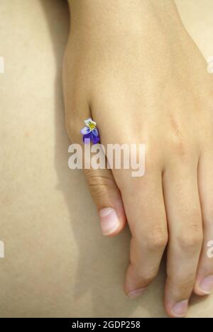 Vertical shot of a woman's hand holding a tiny white and blue flower between her fingers Stock Photo