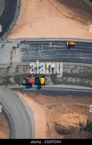 Road Construction of large expressway: road construction equipment works on laying asphalt road junction, aerial top view shot. Stock Photo