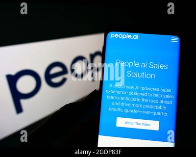 Person holding cellphone with webpage of US artificial intelligence company People.ai Inc. on screen with logo. Focus on center of phone display. Stock Photo