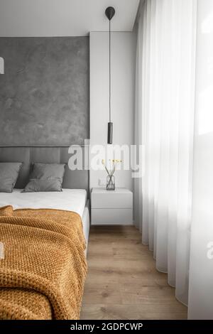 Modern Minimalism Style Bedroom Interior with grey wall and yellow flowers on bedside table Stock Photo