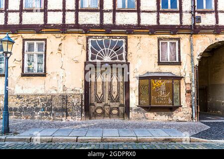 A dilapidated half-timbered house with peeling plaster and a broken fanlight above the door stands on Pölkenstraße in Quedlinburg, Saxony-Anhalt, Germany; a boarded-up shop window beside it bears graffiti, including the words "Frieden" (peace) and "Freiheit" (freedom). The house lies within the town's UNESCO World Heritage area, but appears uninhabited and left to decay. Stock Photo