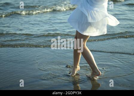 Closeup of a woman's legs as she walks on the wavy waters at the beach Stock Photo