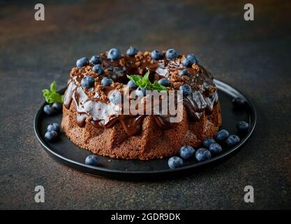 freshly baked chocolate cake decorated with melted chocolate and fresh blueberries on black plate Stock Photo