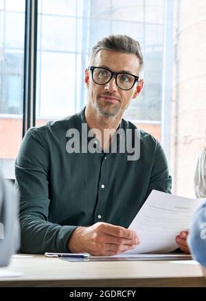 Serious male ceo listening colleague holding papers documents at table meeting. Stock Photo