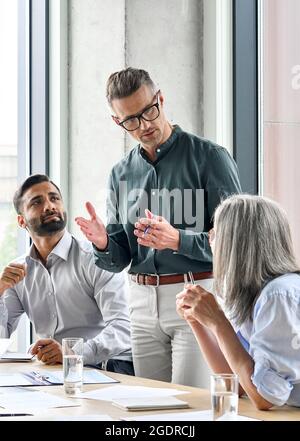 Mature businessman mentor leader talking with managers at meeting in board room. Stock Photo