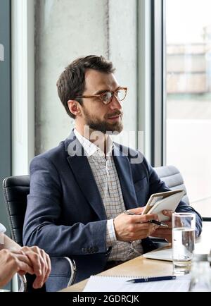 Serious male ceo looking at colleague holding notebook at table meeting. Stock Photo