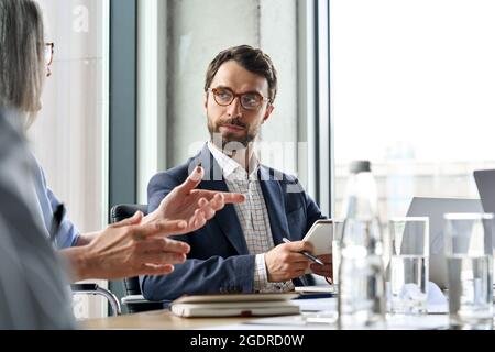Serious male ceo listen to female colleague holding notebook at table meeting. Stock Photo