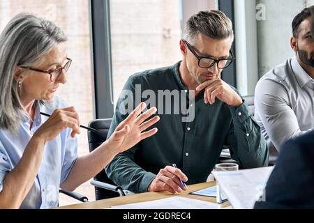 Serious mature partners colleagues discussing contract at table meeting. Stock Photo