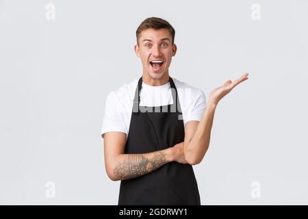 Small business owners, coffee shop and staff concept. Relieved and happy smiling handsome barista rejoicing, raise hand and looking excited, telling Stock Photo