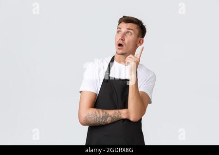 Small business owners, coffee shop and staff concept. Creative handsome barista having an idea, looking upper left corner gasping astounded and raise Stock Photo