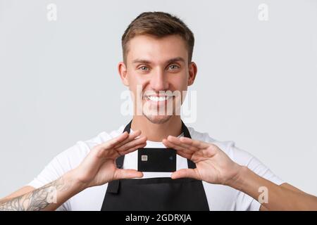 Cafe and restaurants, coffee shop owners and retail concept. Close-up of charismatic smiling waiter, salesman showing credit card, introduce new Stock Photo