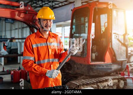 Asian men with large iron wrench in a hand, Powerful Professional Mechanic. Heavy Duty Equipment Maintenance. Industrial Concept. Stock Photo