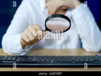 a businessman checks computer equipment with a magnifying glass Internet Information Security Concepts. Stock Photo