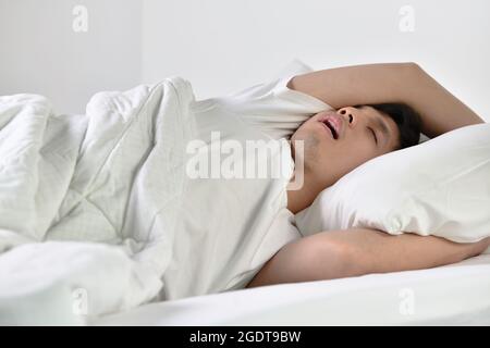 Young Asian man sleeping and snoring loudly lying in the bed Stock Photo