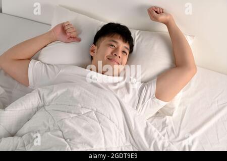 Top view image of happy Asian man waking up in bed in the morning Stock Photo
