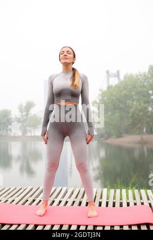 Woman dressed leggings and top with pink mat doing yoga on summer outdoor. Healthy sport lifestyle concept. Active and athletic female exercises Stock Photo