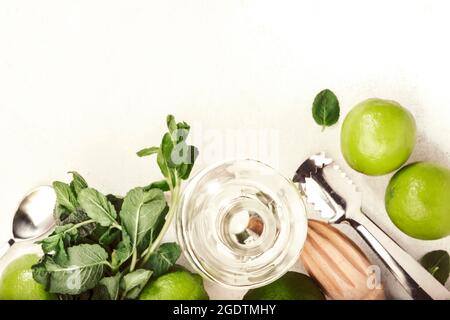 Mojito cocktail making. Mint, lime, ice, white rum, cane sugar - ingredients and bar utensils. Top view, white background. Flat lay Stock Photo