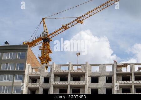 Construction crane on an unfinished residential building against the sun and blue sky. Housing construction, apartment building in the city. Construct Stock Photo