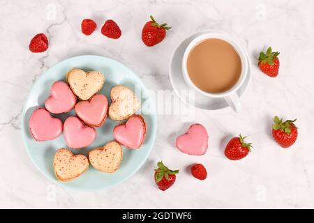 Pink and beige heart shaped French macaron sweets next to coffee cup and strawberry and raspberry fruits Stock Photo