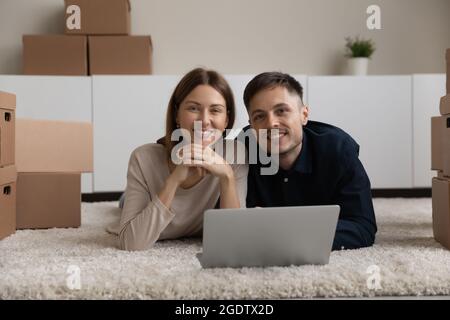 Relaxed couple lying on floor with laptop, cardboard boxes nearby Stock Photo
