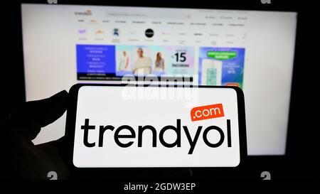 Person holding smartphone with logo of Turkish e-commerce company Trendyol on screen in front of website. Focus on phone display. Stock Photo