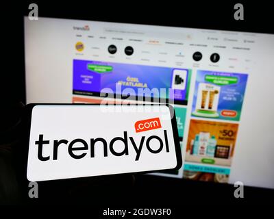 Person holding cellphone with logo of Turkish e-commerce company Trendyol on screen in front of business webpage. Focus on phone display. Stock Photo