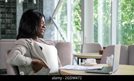 African-American lady types on laptop reading papers in cafe Stock Photo