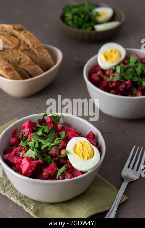 Russian salad vinaigrette in plates with boiled egg and black bread, salad of boiled potatoes and carrots, beetroot and pickled vegetables, cucumber Stock Photo