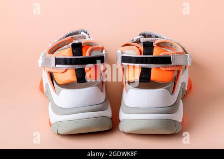 Women's, fashionable, sports sandals with orange accents on a pink background. New youth shoes for girls. Back view. Stock Photo