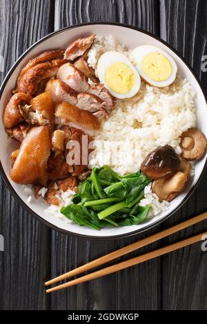 Stewed pork leg with rice, eggs and herb Thai Khao Kha Moo closeup in the bowl on the table. Vertical top view from above Stock Photo