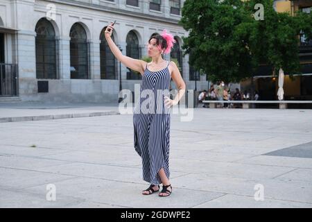 Young caucasian woman with pink hair taking a selfie in street with earbuds. Stock Photo
