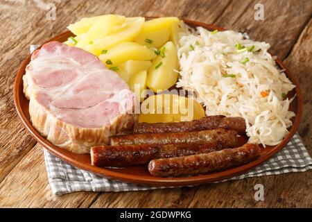 Smoked pork neck and sausages with cabbage Sauerkraut boiled potatoes and mustard closeup in the plate on the table. Horizontal Stock Photo