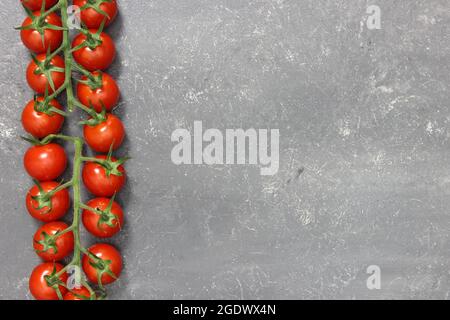 small red vine or cocktail tomatoes on a panicle lying on a gray slate background Stock Photo