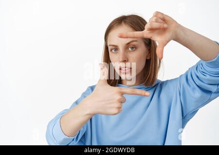 Image of serious creative blond woman searching angle for shot, look through hand frames with furrowed eyebrows, thinking, working on perfect photo Stock Photo