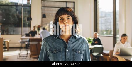 Portrait of freelancer standing in co-working space. Confident businesswoman looking at camera. Stock Photo