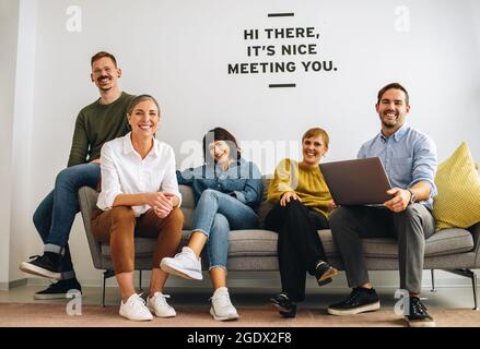Cheerful executives sitting together on sofa and smiling at camera. Happy business team looking at camera while sitting together in lobby. Stock Photo