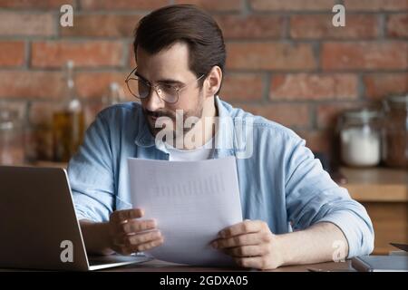 Serious millennial man work on laptop with paperwork Stock Photo